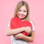 Weibliches Mädchen mit Liebevollem Ausdruck hält rotes Plüschtier Herzlichkeit und Schutz symbolisiert, geeignet für Themen wie EMF-Schutz, Elektrosmog, Gesundheit und Wohlbefinden.