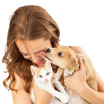 Frau hält Welpe und Kätzchen, Hund leckt Gesicht.