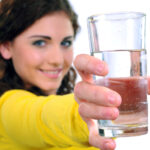 Frau hält Wasser im Glas, Nahaufnahme, lächelnd