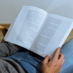 Junge Person liest ein Buch mit Notizen, Kaffee auf dem Schoß, im Fokus auf elektromagnetische Felder (EMF) Schutz und gesunde Lernumgebung.