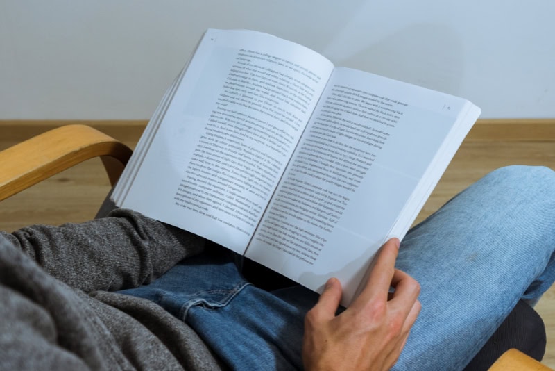 Persona joven lee un libro con notas, café en el regazo, enfocado en la protección contra campos electromagnéticos (EMF) y un entorno de aprendizaje saludable.