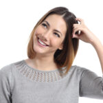 Frau denkt nach, während sie sich die Haare berührt, symbolisiert Bewusstsein für elektromagnetische Felder und Schutz vor EMF-Belastung.