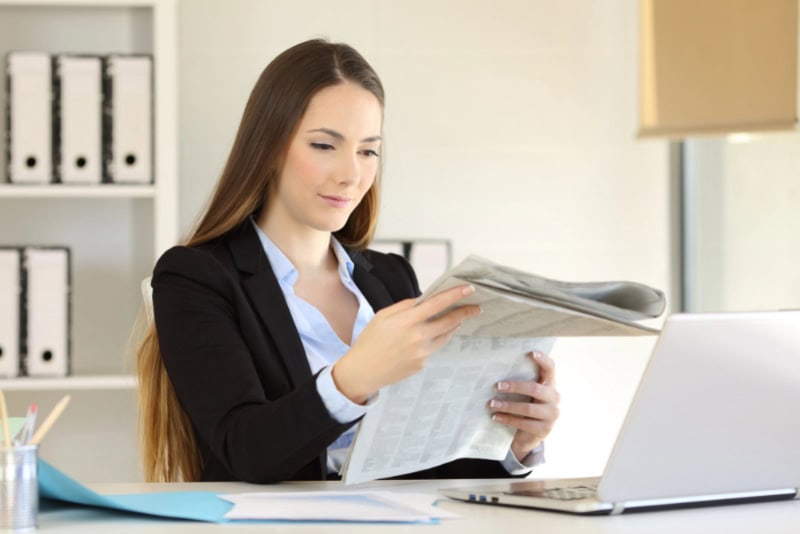 Mujer de negocios lee el periódico en la oficina, rodeada de un entorno de trabajo moderno, con enfoque en la protección de la salud contra la radiación electromagnética.