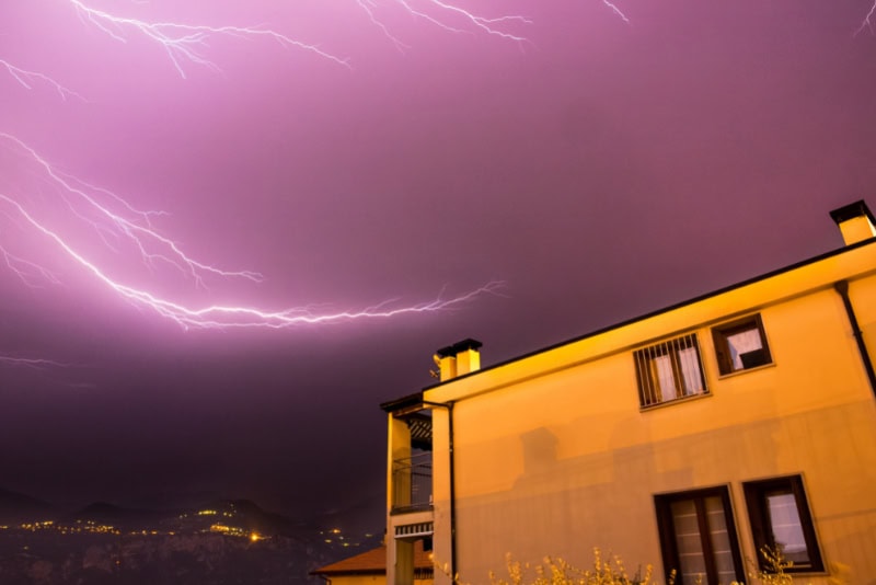 Fulmine durante un temporale notturno sopra una casa, con cielo scuro e scarica elettrica.