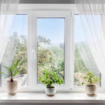 Modern window with white tulle curtains and potted plants, ideal for natural light penetration and room design. Perfect for EMF protection and healthy living.